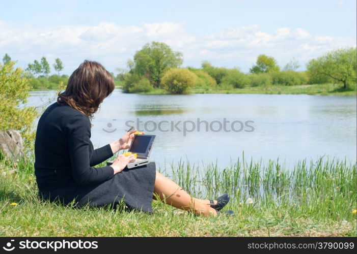 Woman typing on a laptop outside in a meadow. Blue sky with clouds.