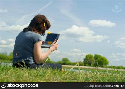 Woman typing on a laptop outside in a meadow. Blue sky with clouds.