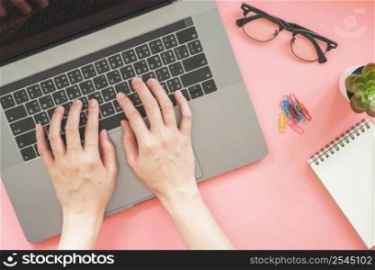 woman typing on laptop in pink pastel colourful office with accessories