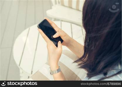 Woman typing text message on smart phone in a cafe. Cropped image of young woman sitting at a table with a coffee using mobile phone.