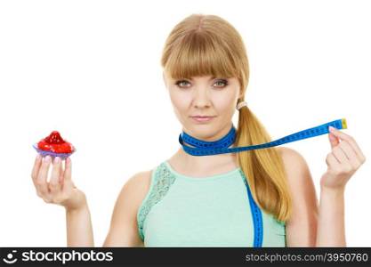 Woman undecided with blue measuring tape around her neck holds in hand cake cupcake, trying to resist temptation. Weight loss diet dilemma gluttony concept.