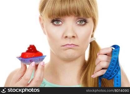 Woman undecided with blue measuring tape holds in hand cake cupcake, trying to resist temptation. Weight loss diet dilemma gluttony concept.