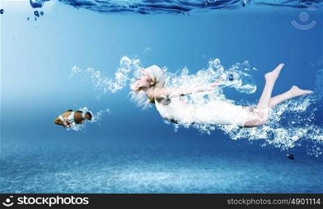 Woman underwater. Young woman in white dress swimming under water
