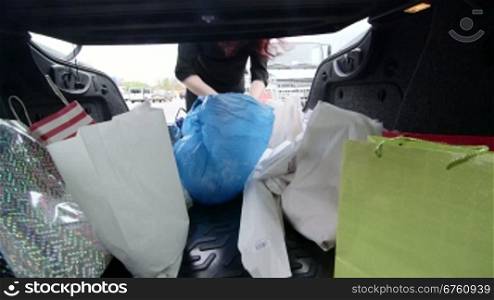 Woman unloads groceries in plastic and paper bags into the trunk of her car after shopping in supermarket