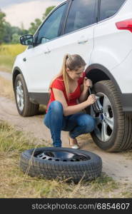 Woman unscrewing nuts on car flat wheel at field