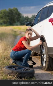 Woman unscrewing nuts on car flat wheel at field