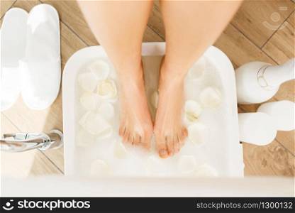 Woman uses a foot bath with white rose petals, beauty salon. Professional beautician service, female customer, skin and body care in spa studio