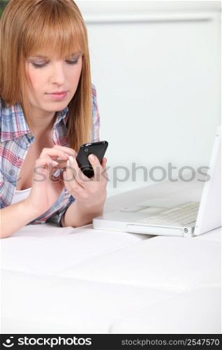 Woman using a cellphone while sitting at a laptop