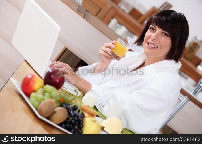 Woman using a laptop while eating a fruity breakfast