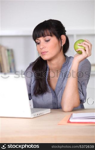 Woman using a laptop with an apple in her hand