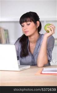 Woman using a laptop with an apple in her hand