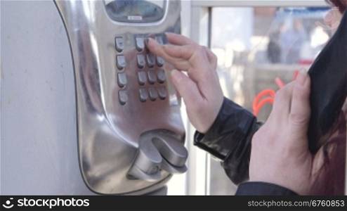 Woman using a public pay phone booth on a city street close-up