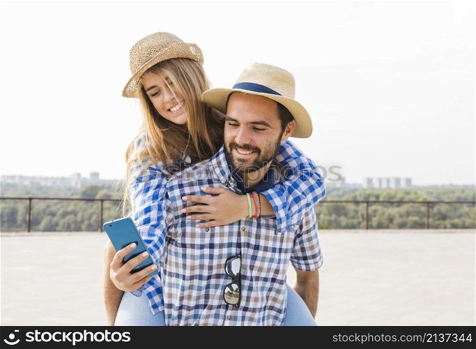 woman using cellphone while having piggyback her boyfriend s back