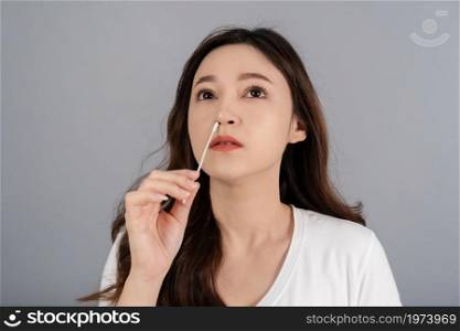 woman using coronavirus(covid-19) rapid antigen self test kit (atk) at home with a cotton nasal swab