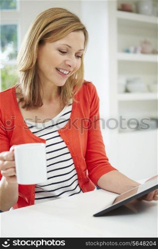 Woman Using Digital Tablet At Home In Kitchen