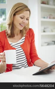 Woman Using Digital Tablet At Home In Kitchen