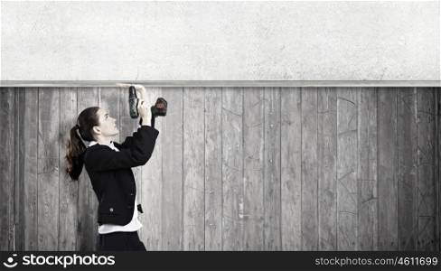 Woman using drill. Young businesswoman fixing cement banner with drill