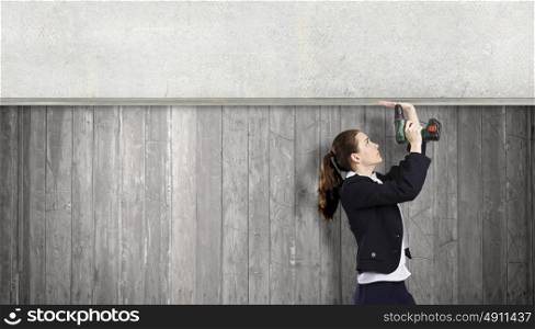 Woman using drill. Young businesswoman fixing cement banner with drill