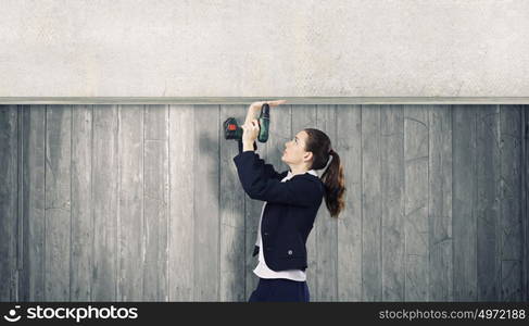 Woman using drill. Young businesswoman fixing cement banner with drill