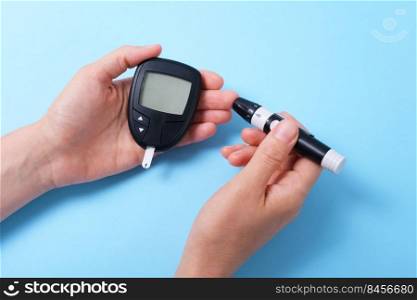 Woman using glucometer, checking blood sugar level. Diabetes concept on blue background. The hand holds the glucometer and pricks the finger with a lancet.. Woman using glucometer, checking blood sugar level. Diabetes concept on blue background. The hand holds the glucometer and pricks the finger with a lancet