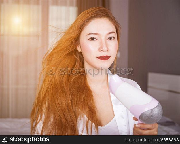 woman using hair dryer in the bedroom with soft light