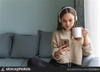 woman using headphones smartphone home while having coffee during pandemic