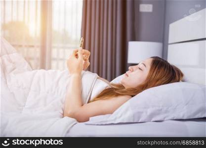 woman using her smartphone on bed in the bedroom with soft light