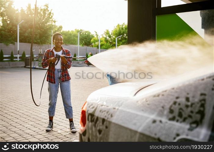 Woman using high pressure water gun with foam, hand car wash station. Car-wash industry or business. Female person cleans her vehicle from dirt outdoors. Woman using water gun with foam, hand car wash