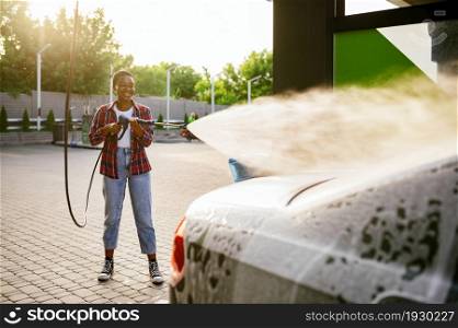 Woman using high pressure water gun with foam, hand car wash station. Car-wash industry or business. Female person cleans her vehicle from dirt outdoors. Woman using water gun with foam, hand car wash