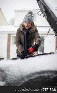 Woman Using Jumper Cables On Car Battery On Snowy Day