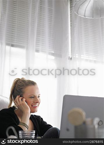 Woman using laptop and mobile phone sitting at desk low angle view