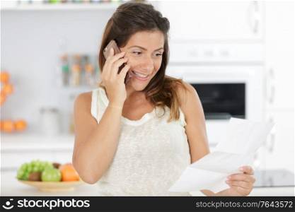 woman using laptop and talking on mobile phone in kitchen
