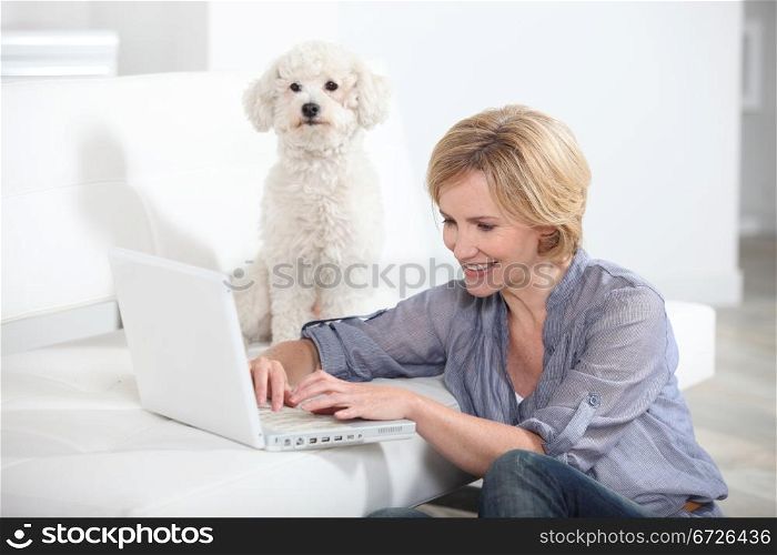Woman using laptop computer next to small white dog