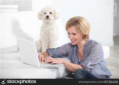 Woman using laptop computer next to small white dog