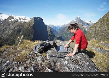 Woman using laptop on mountain peak