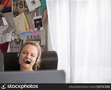 Woman using laptop wearing headset sitting at desk