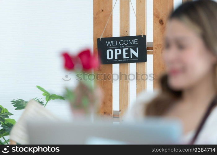 Woman using laptop with open sign in floral shop. Business concept.