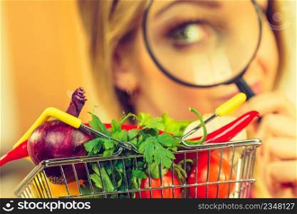 Woman using magnifying glass loupe, investigating shopping basket with many colorful vegetables. Healthy eating lifestyle, nutrients vegetarian food, searching for pesticides and chemicals.. Woman investigating shopping backet with vegetables