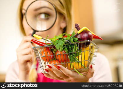 Woman using magnifying glass loupe, investigating shopping basket with many colorful vegetables. Healthy eating lifestyle, nutrients vegetarian food, searching for pesticides and chemicals.. Woman investigating shopping backet with vegetables