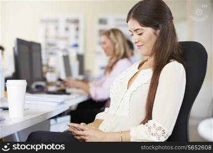 Woman Using Mobile Phone At Desk In Busy Creative Office