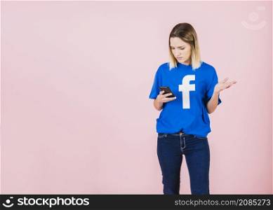 woman using mobile phone shrugging against pink background