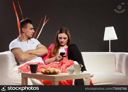 Woman using mobile phone texting and bored man.. Woman using mobile phone texting and sending messages and bored man sitting on sofa at home. Wife addicted to new technology surfing internet. Bad relationship.