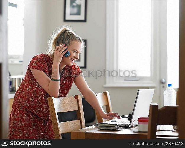 Woman using mobile phone while using laptop in dining room side view