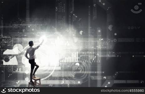 Woman using modern technologies. Back view of businesswoman standing on chair and reaching icon on virtual screen