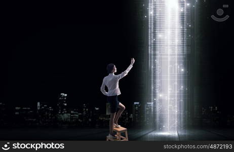 Woman using modern technologies. Back view of businesswoman standing on chair and reaching icon on virtual screen