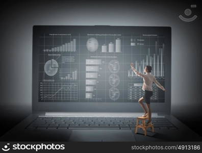 Woman using modern technologies. Back view of businesswoman standing on chair and reaching laptop screen