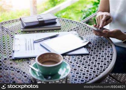 woman using smart phone and coffee beside on a wooden table in garden, warm sunlight