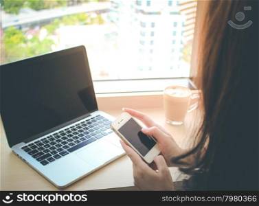 Woman using smart phone and laptop in the cafe with flare light from window