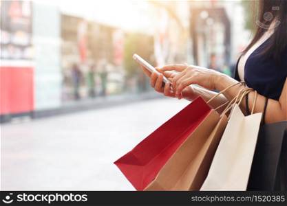 Woman using smartphone and holding shopping bag while standing on the mall background
