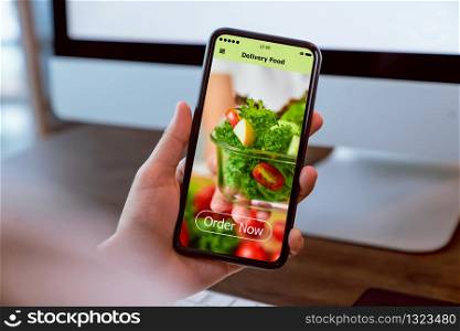 Woman using smartphone and touching application screen for ordering salad online on the table at office.